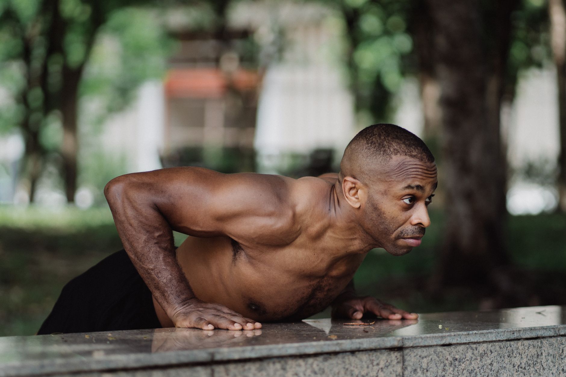 A muscular man performing push-ups on a concrete surface in a park, showcasing strength and fitness.