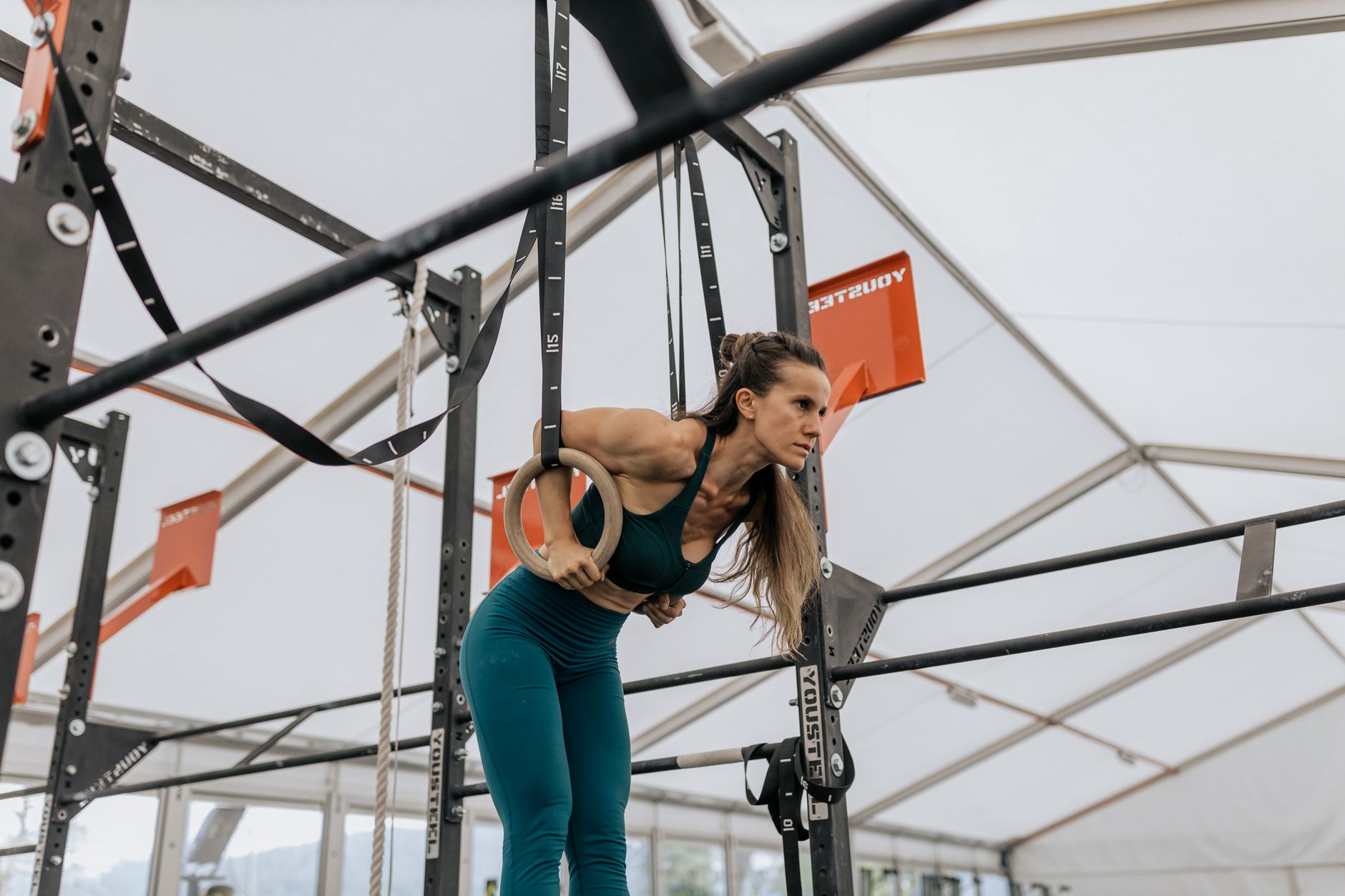 A focused woman exercising with rings in a modern indoor gym setup.