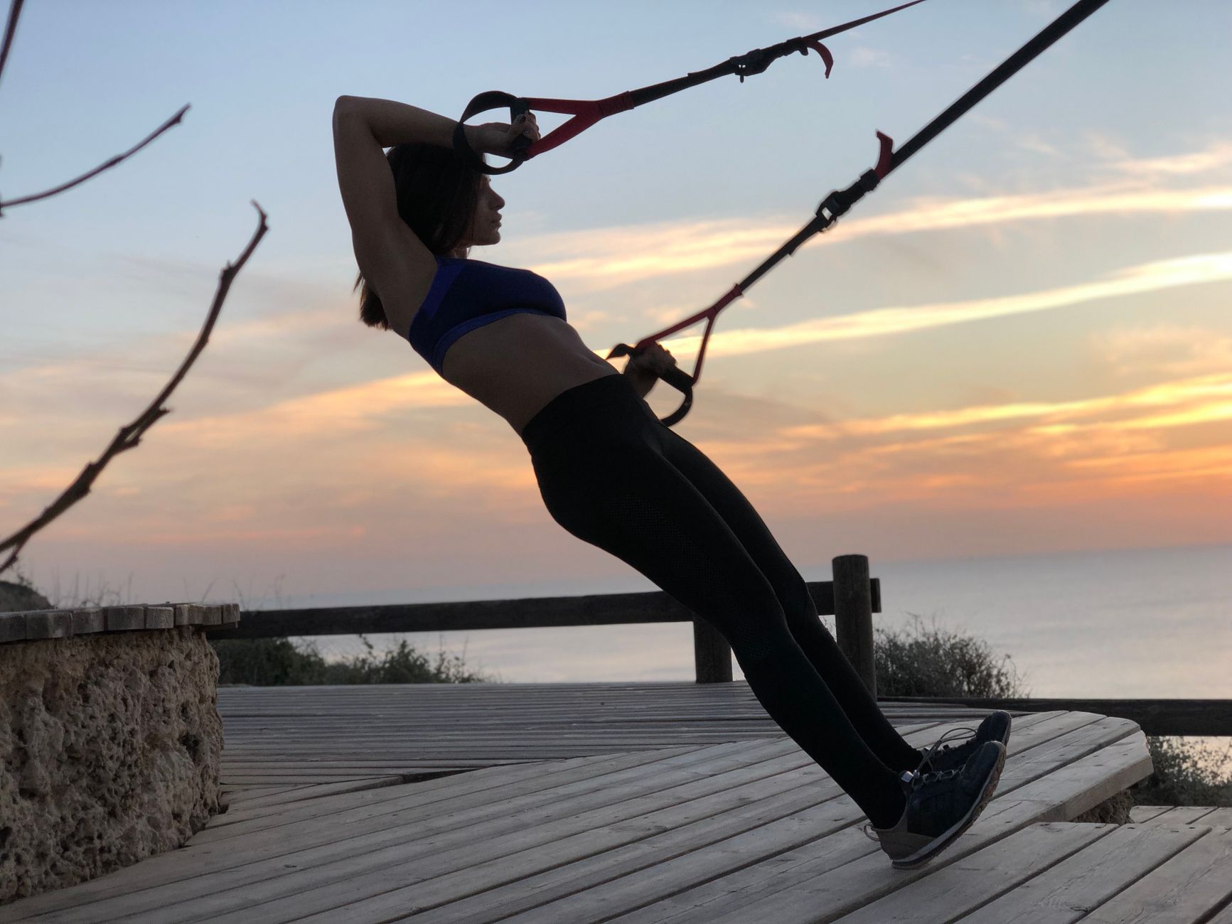 A woman exercising with TRX bands at sunset on Herzliya Beach, Israel.