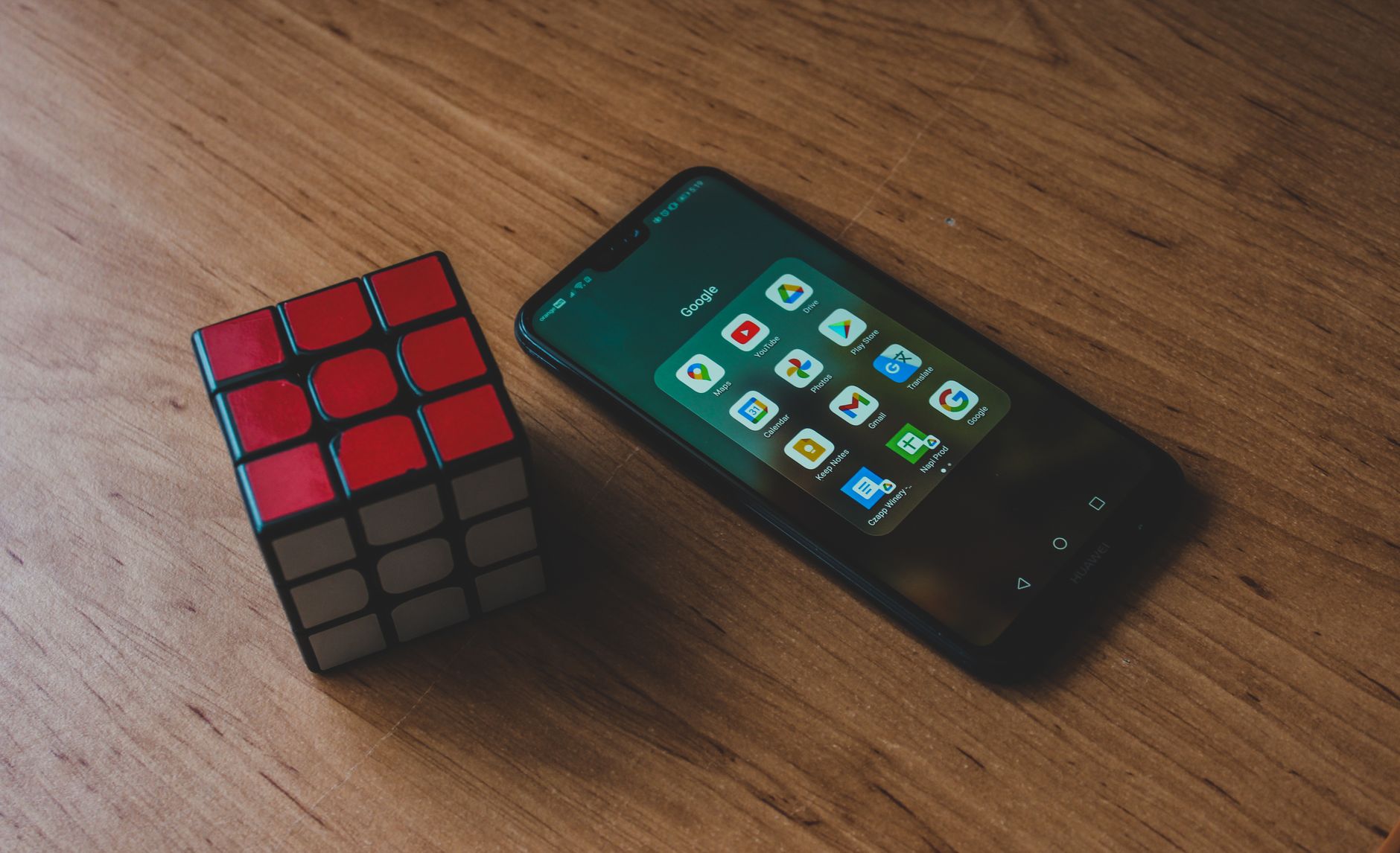 Close-up of smartphone with apps and a Rubik's Cube on a wooden table. Ideal for tech and leisure topics.