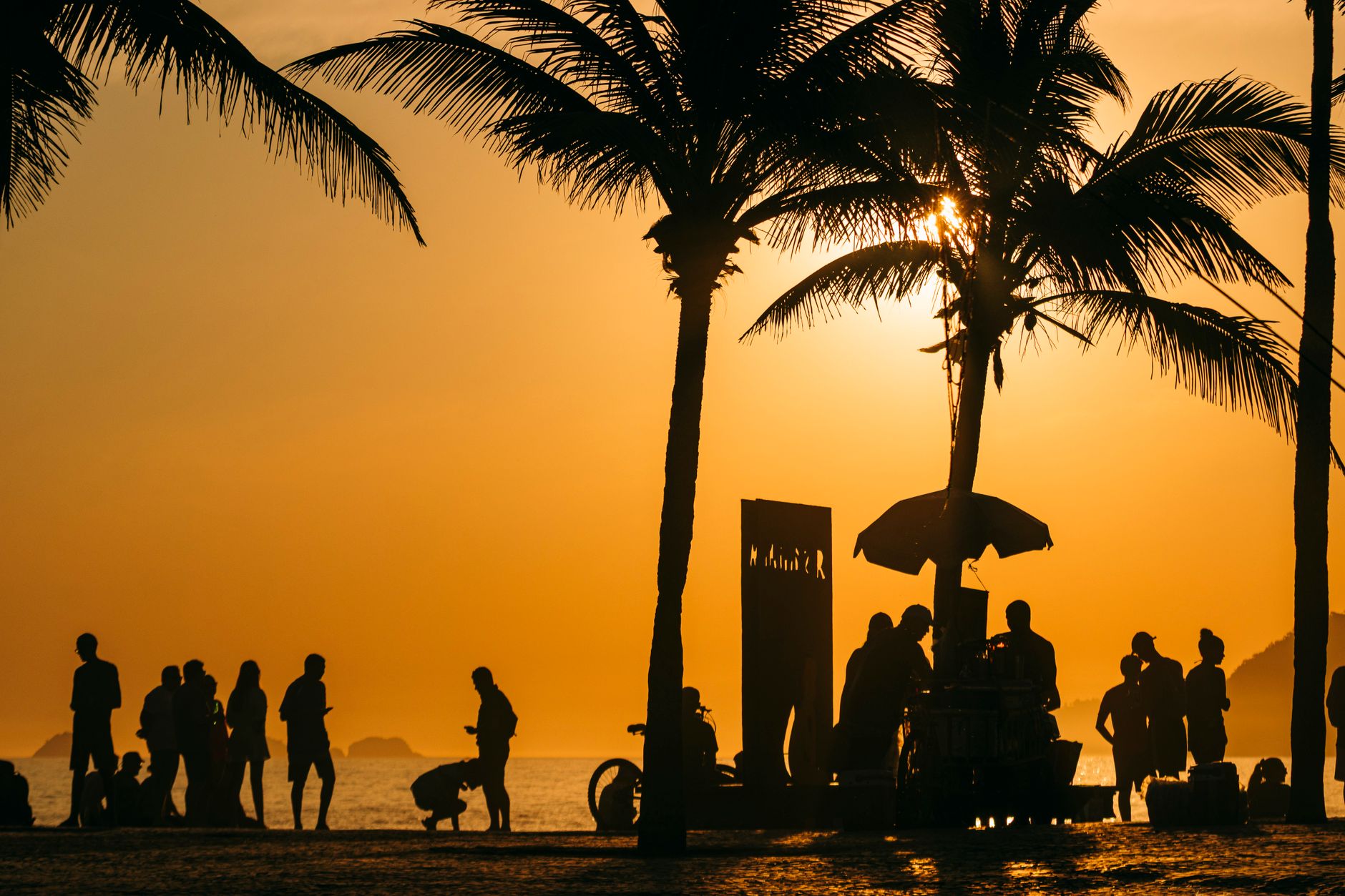Silhouetted people and palm trees at sunset on a Rio de Janeiro beach, capturing the vibrant summer atmosphere.