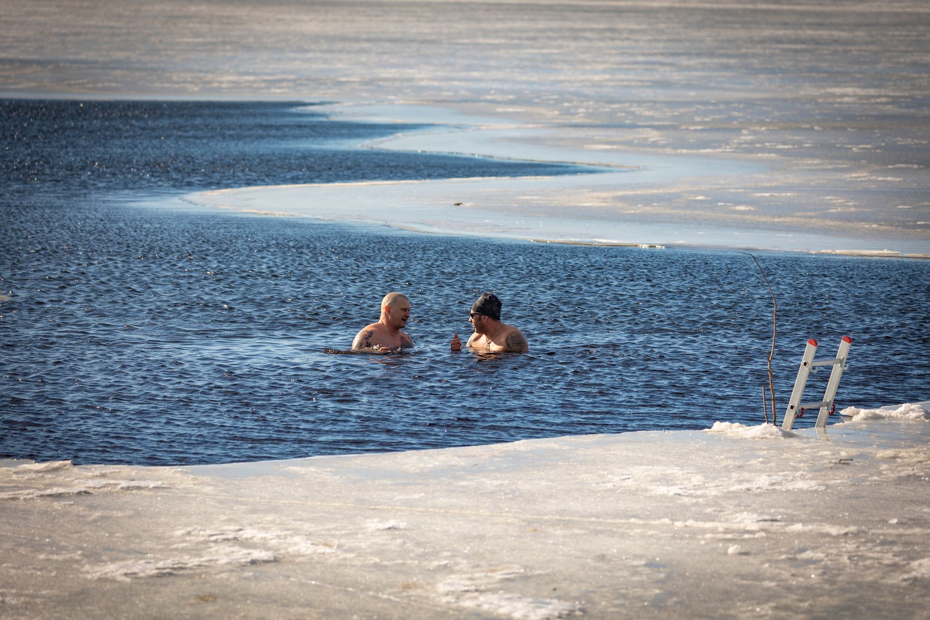 Two men brave the cold for a swim in a partially frozen lake during winter.