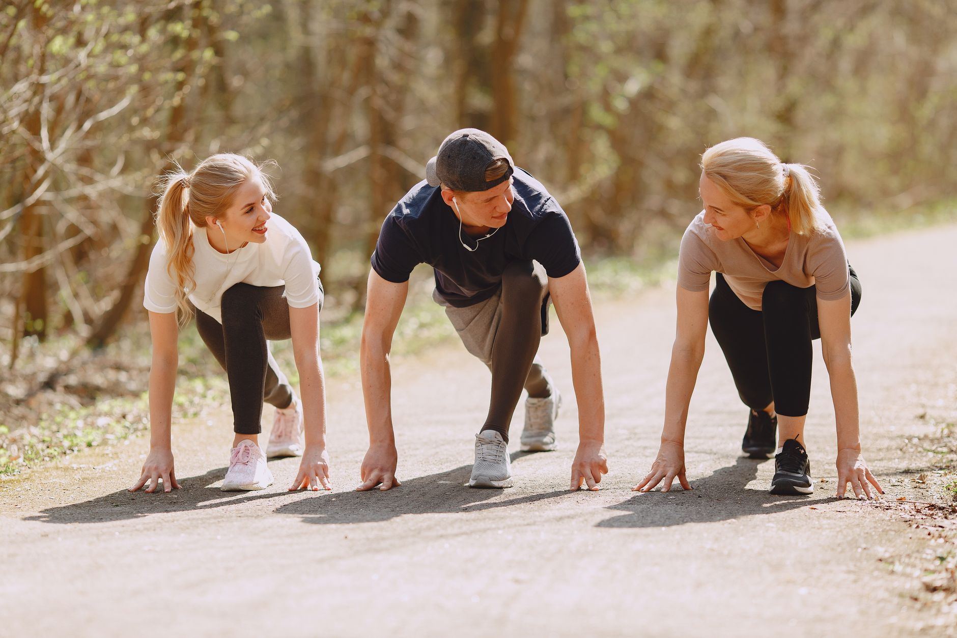 Group of cheerful athletes in sportswear in ready pose for sprinting together during fitness workout and running in spring park