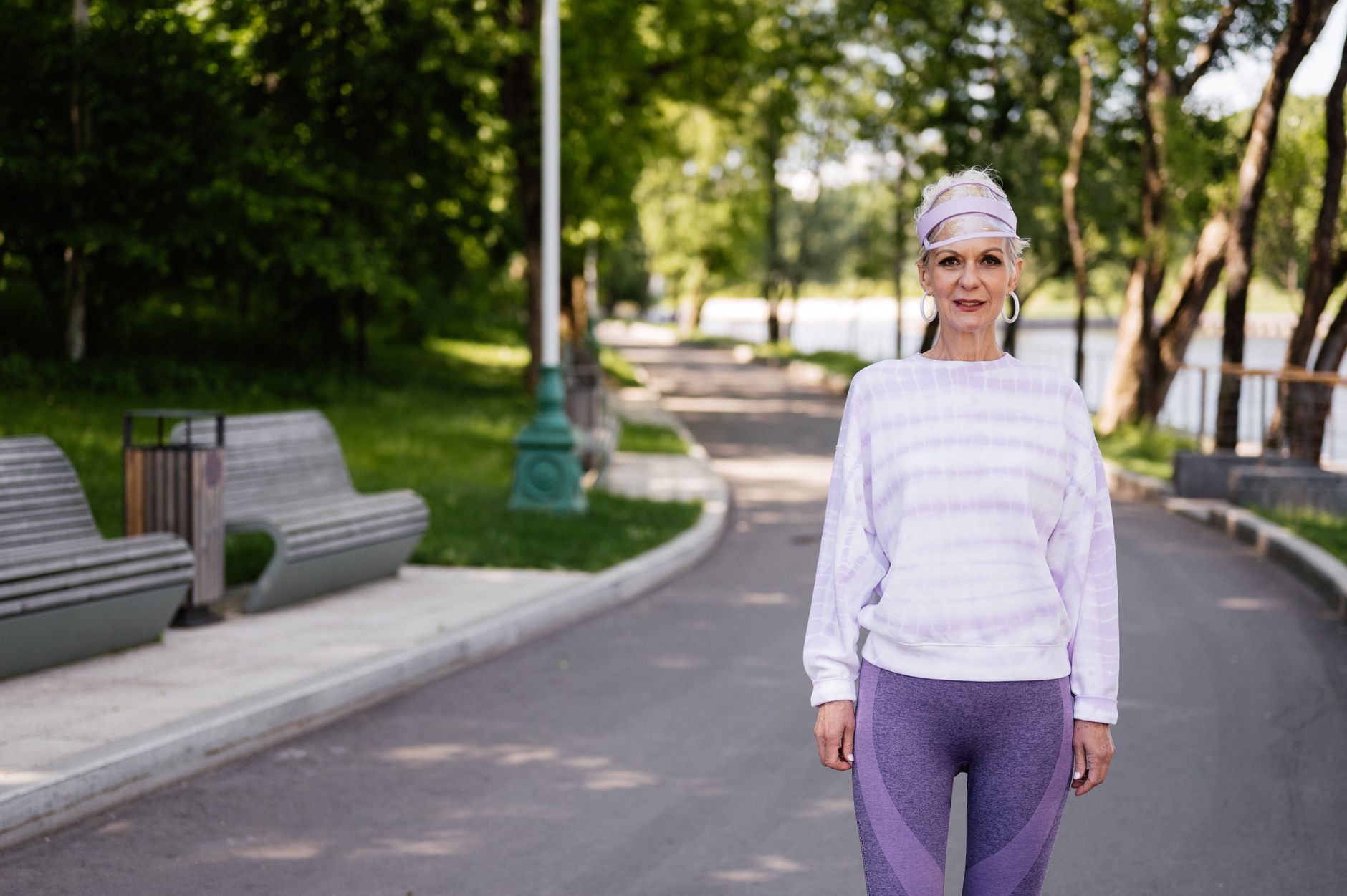 Senior woman in activewear enjoying a walk in a sunny park setting.