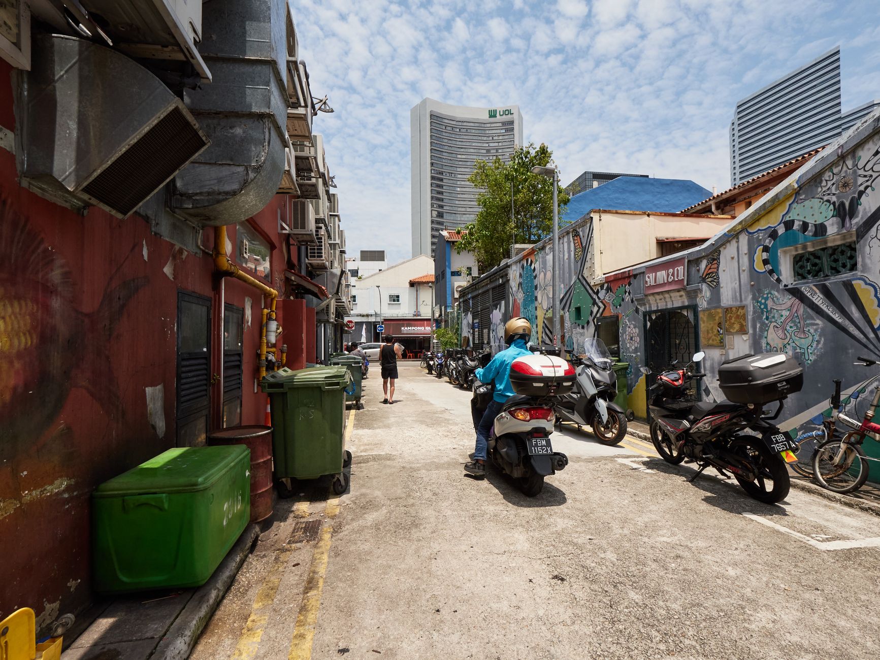 Colorful urban alley in Singapore featuring street art, motorcycles, and modern buildings in the background.