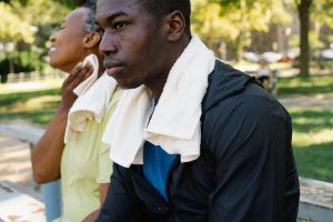 Two adults relaxing on a park bench with towels after a workout under the summer sun.