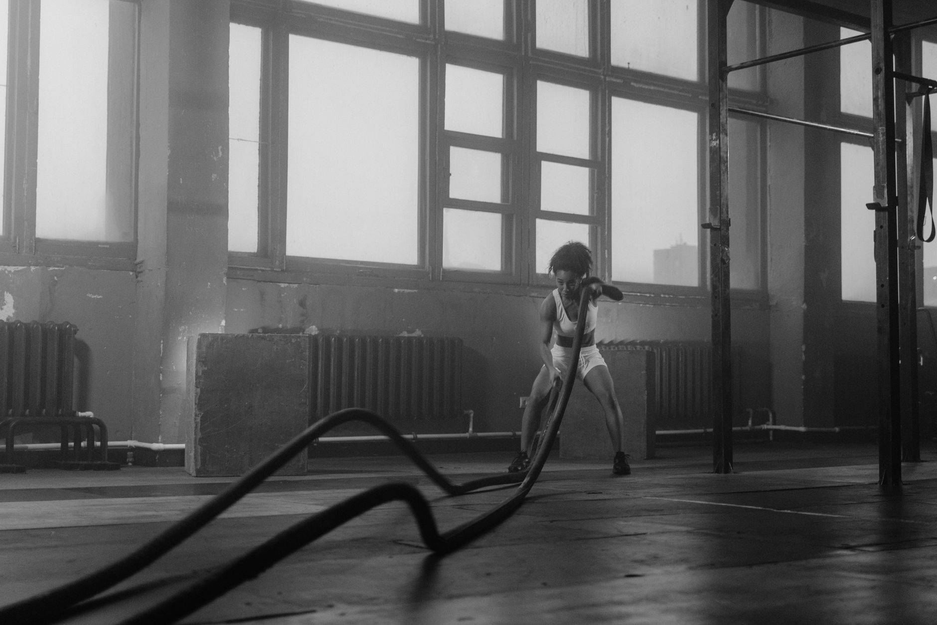 Black woman in gym performing an intense battle ropes workout, highlighting strength and fitness.