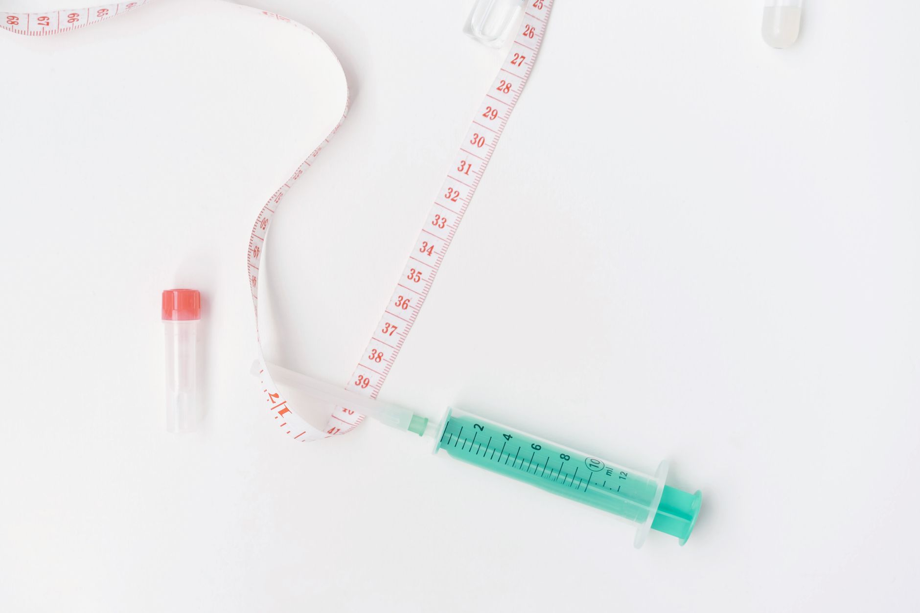 Flat lay of medical supplies with tape measure and syringe on white background, symbolizing healthcare.