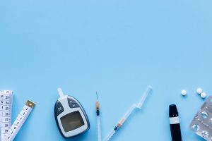 Flat lay of diabetes management tools including glucose meter, syringe, and pills on blue background.