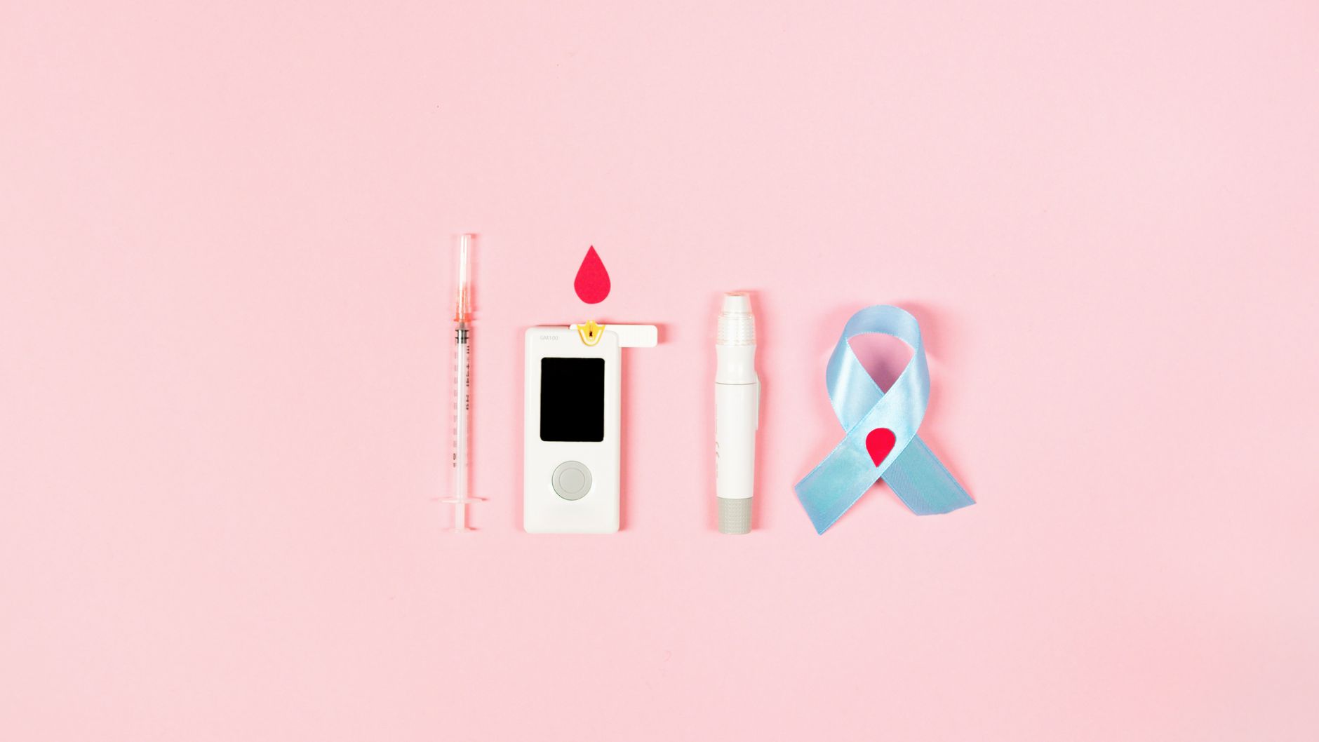 Glucometer, syringe, lancet pen, and ribbon symbolizing diabetes awareness on pink background.