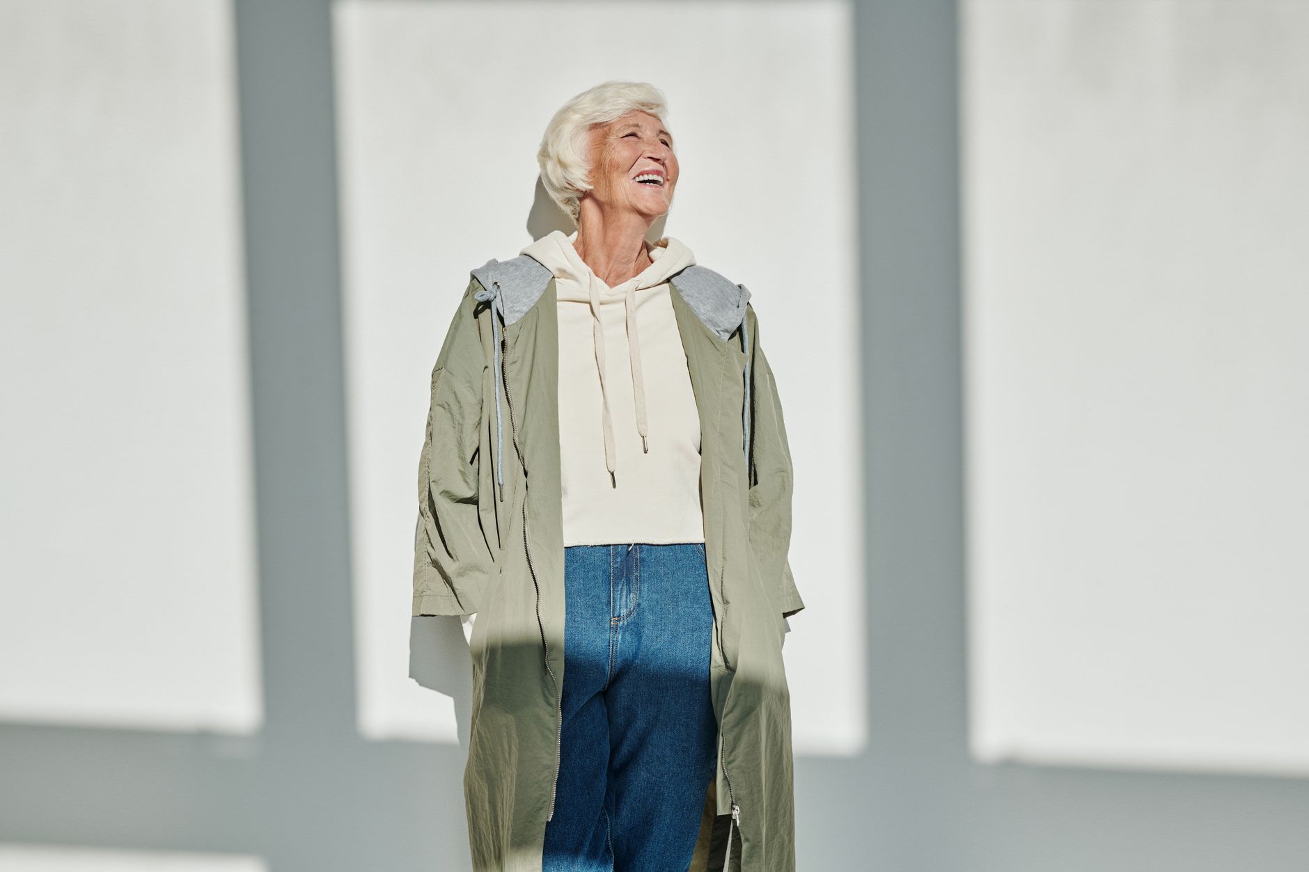 Senior woman smiling while wearing a chic coat and jeans, embracing modern fashion with a joyful expression.