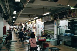 A lively indoor food court with people enjoying meals at various stalls.