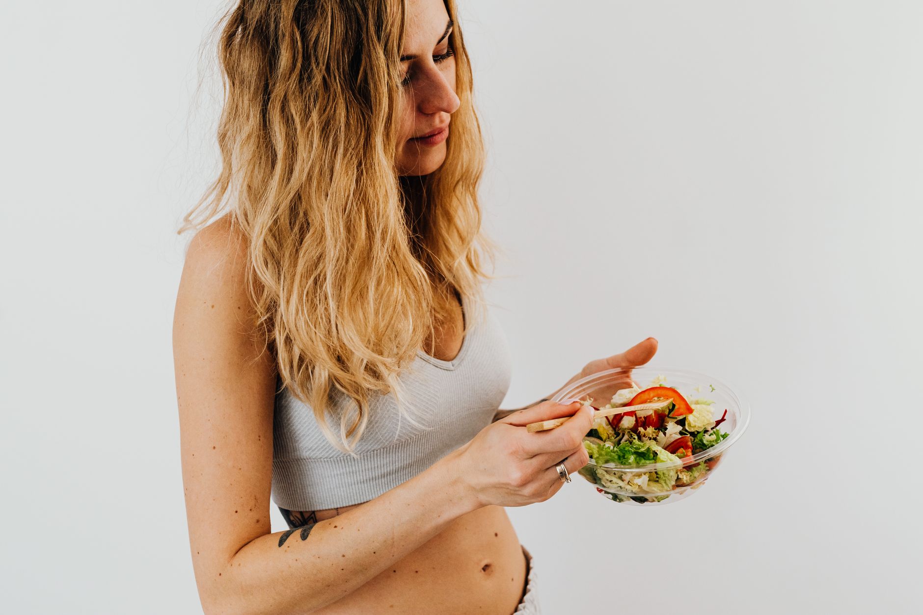 A caucasian woman in a sports bra enjoying a fresh salad, embodying healthy eating and lifestyle.
