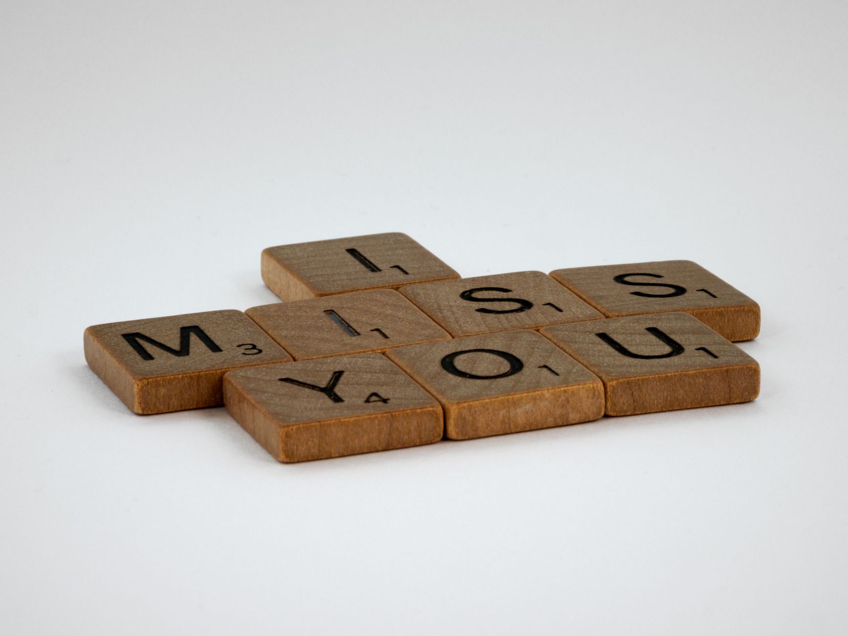 Close-up of Scrabble tiles spelling 'I Miss You' on a white surface with ample copy space.