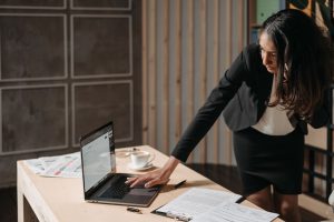 Professional businesswoman multitasking at an office desk, focused on her tasks with a laptop.