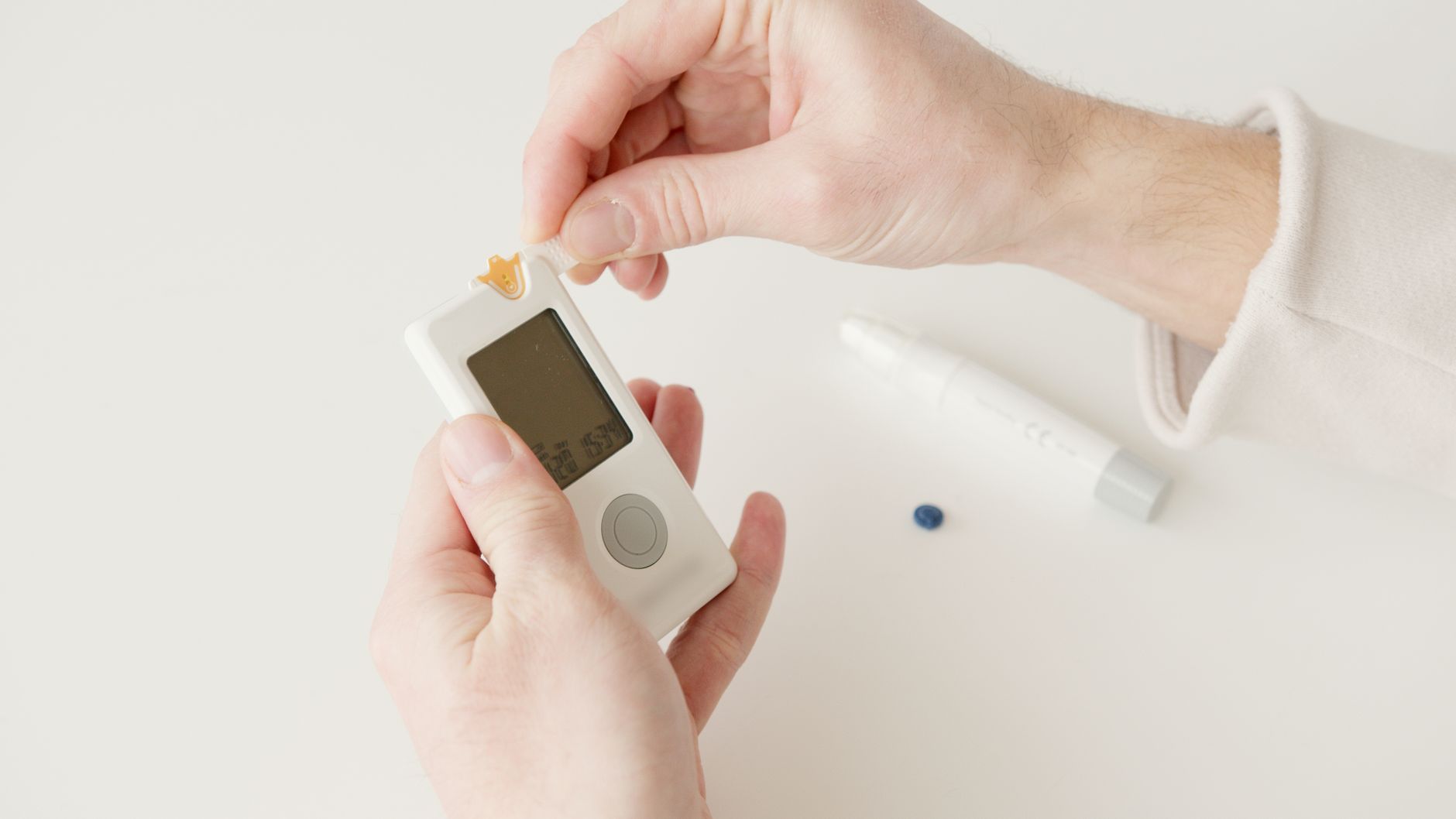 Close-up image of hands checking blood glucose level using a glucometer, featuring testing supplies on a white background.