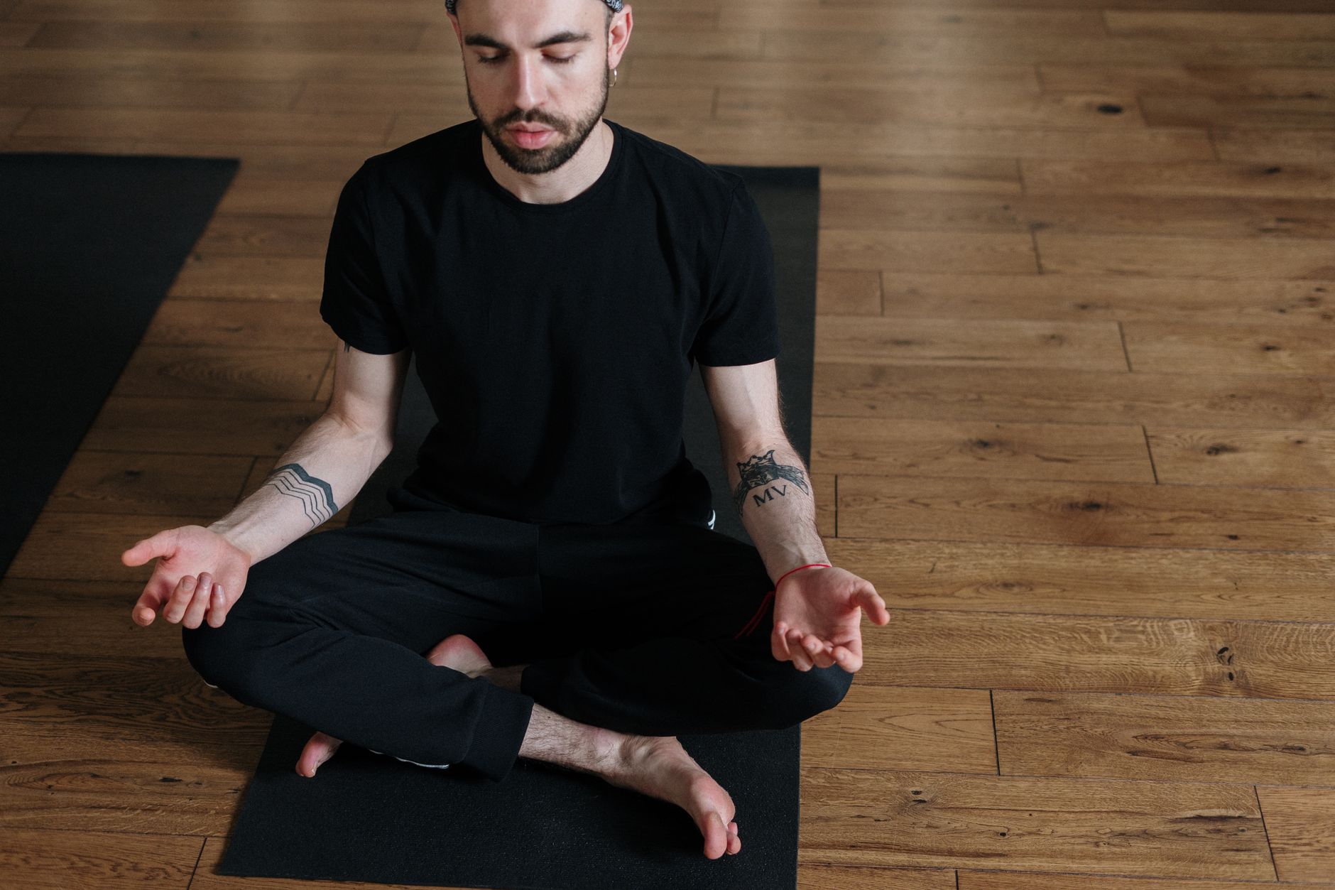 Adult man practicing meditation in lotus pose indoors, focusing on relaxation and mindfulness.