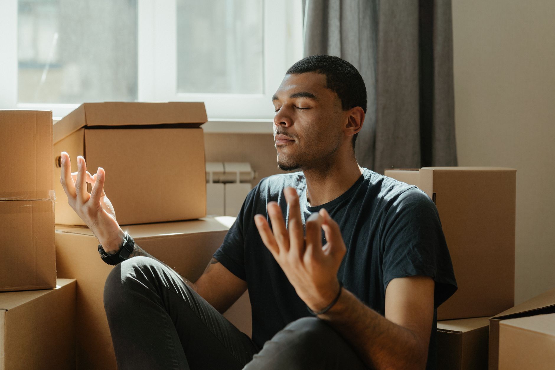 A young man practices meditation surrounded by cardboard boxes during a move.