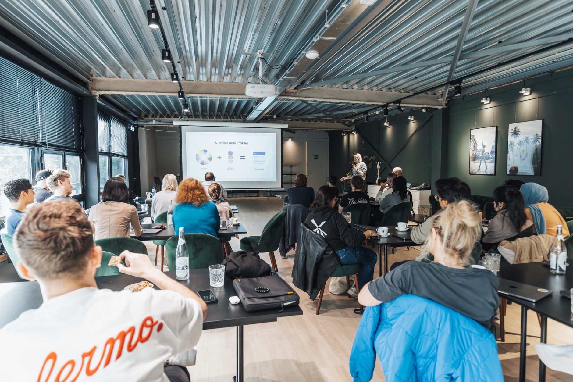 A diverse group attends a corporate presentation in a stylish industrial room, showcasing collaboration.