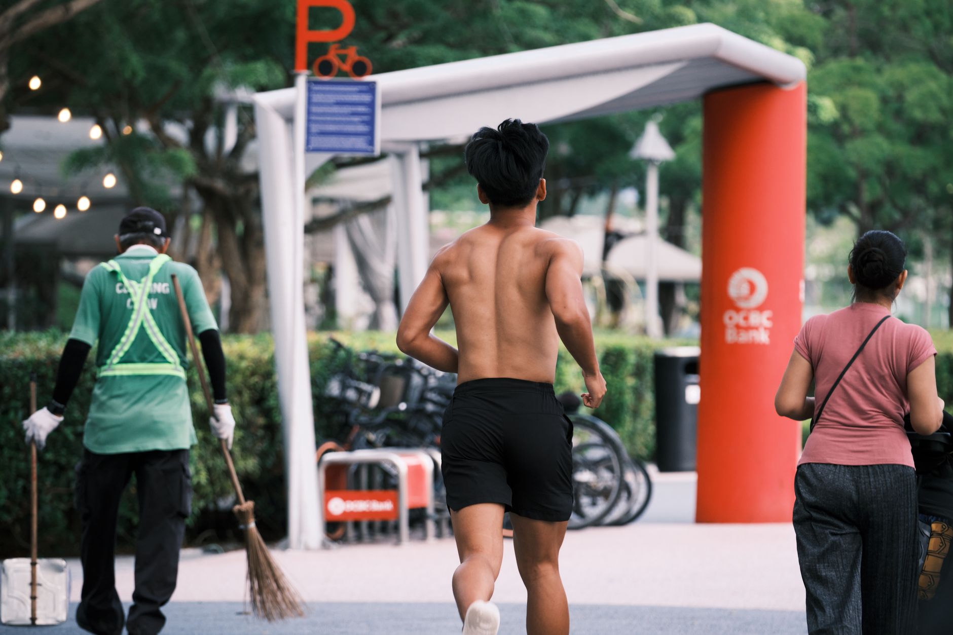 A shirtless man jogging on a sunny day in Singapore city amidst pedestrians and urban landscape.