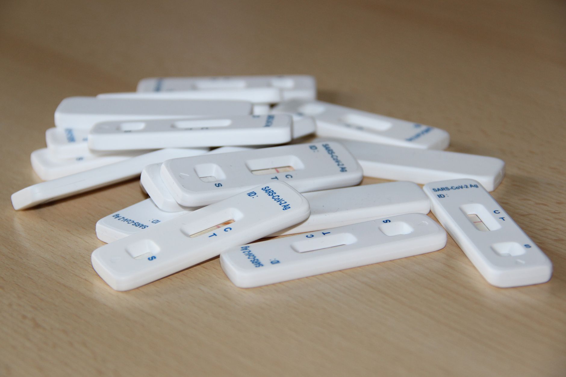 Close-up of several Covid-19 rapid test kits scattered on a wooden table.