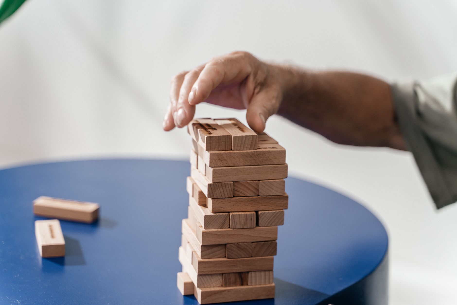 A close-up shot of a hand stacking wooden Jenga blocks on a blue table indoors.
