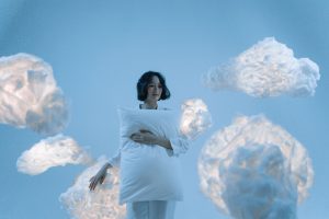 A serene portrait of a woman holding a pillow surrounded by soft clouds, evoking a dreamlike atmosphere.