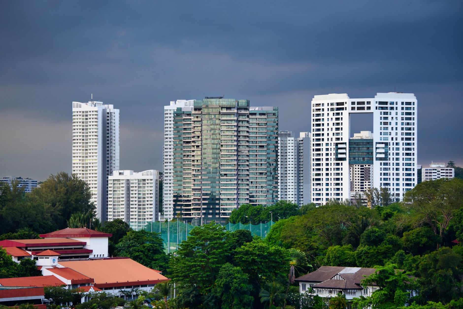 Skyscrapers in Singapore surrounded by vibrant greenery under a dramatic sky.