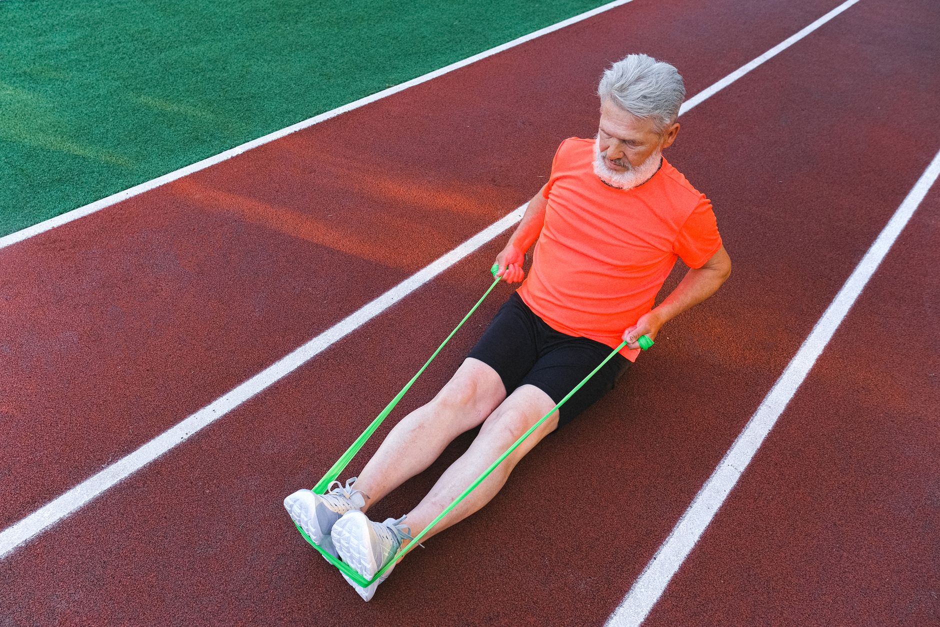 From above of diligent sporty male training with elastic rubber on racetrack in stadium
