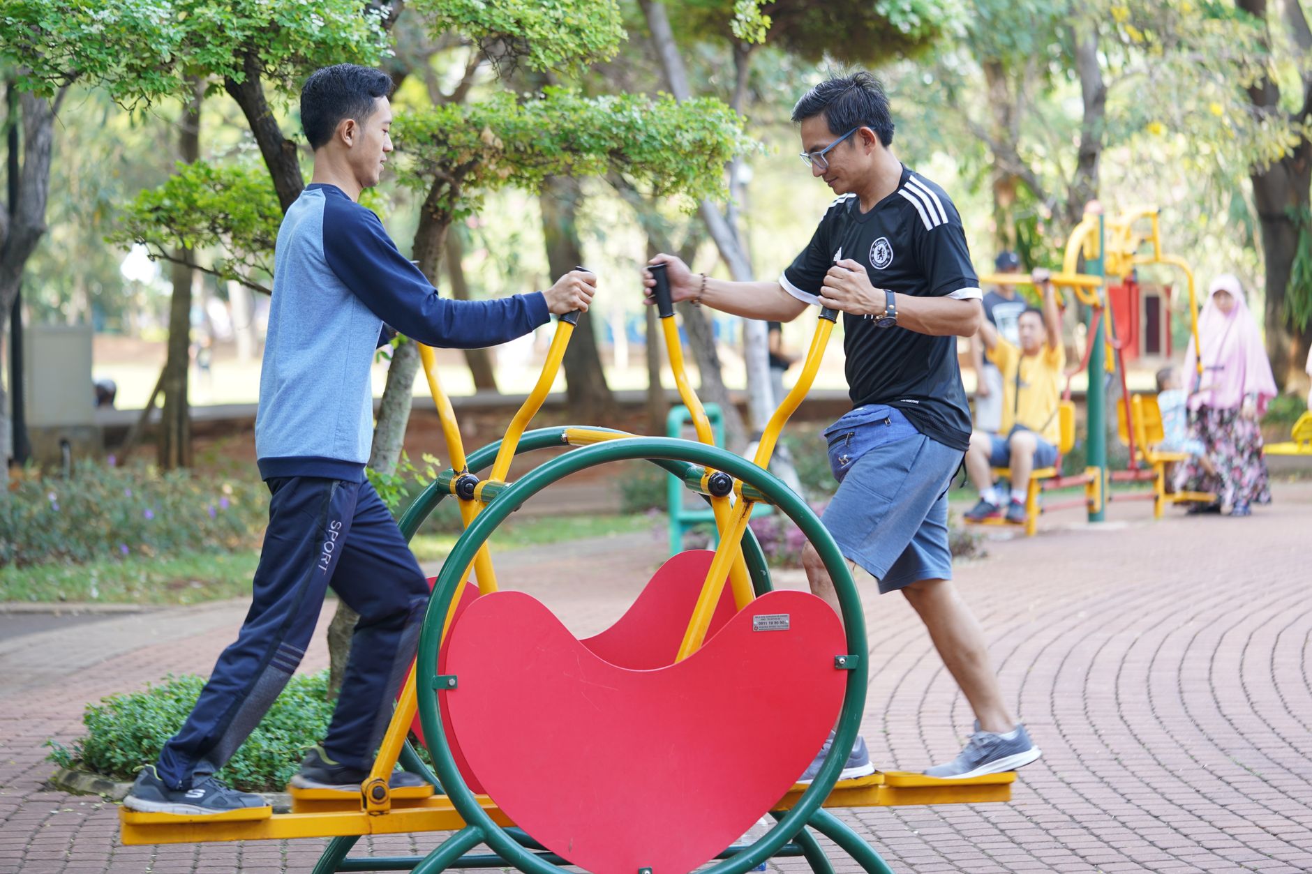 Two adults using outdoor gym equipment in a leafy park setting, enjoying fitness and nature.