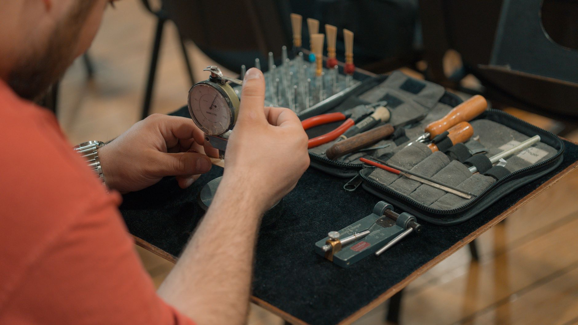 A craftsman using a dial indicator tool, surrounded by other hand tools on a workshop table.